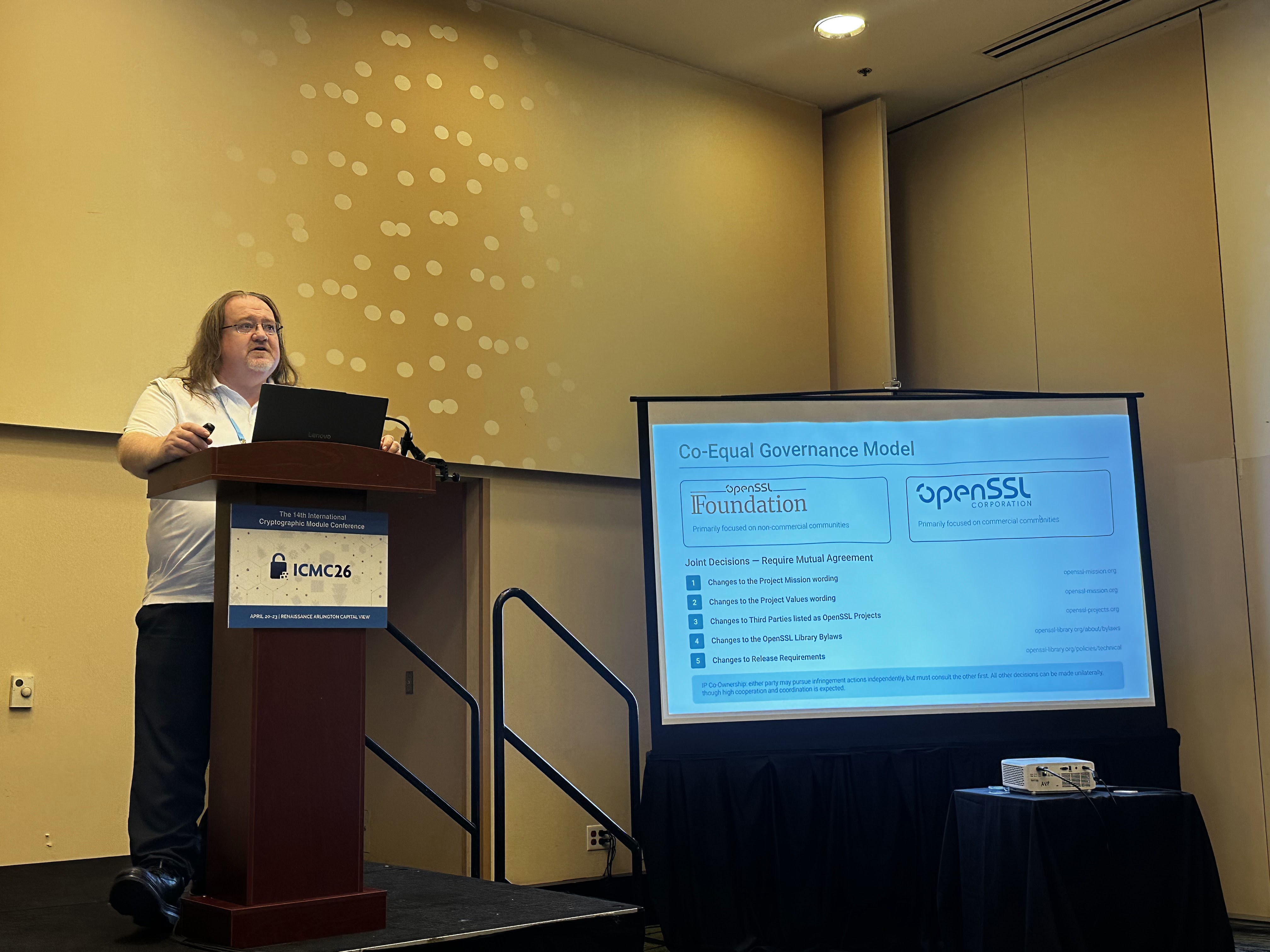 Tim Hudson at the podium in Studio E with the OpenSSL Co-Equal Governance slide on screen.