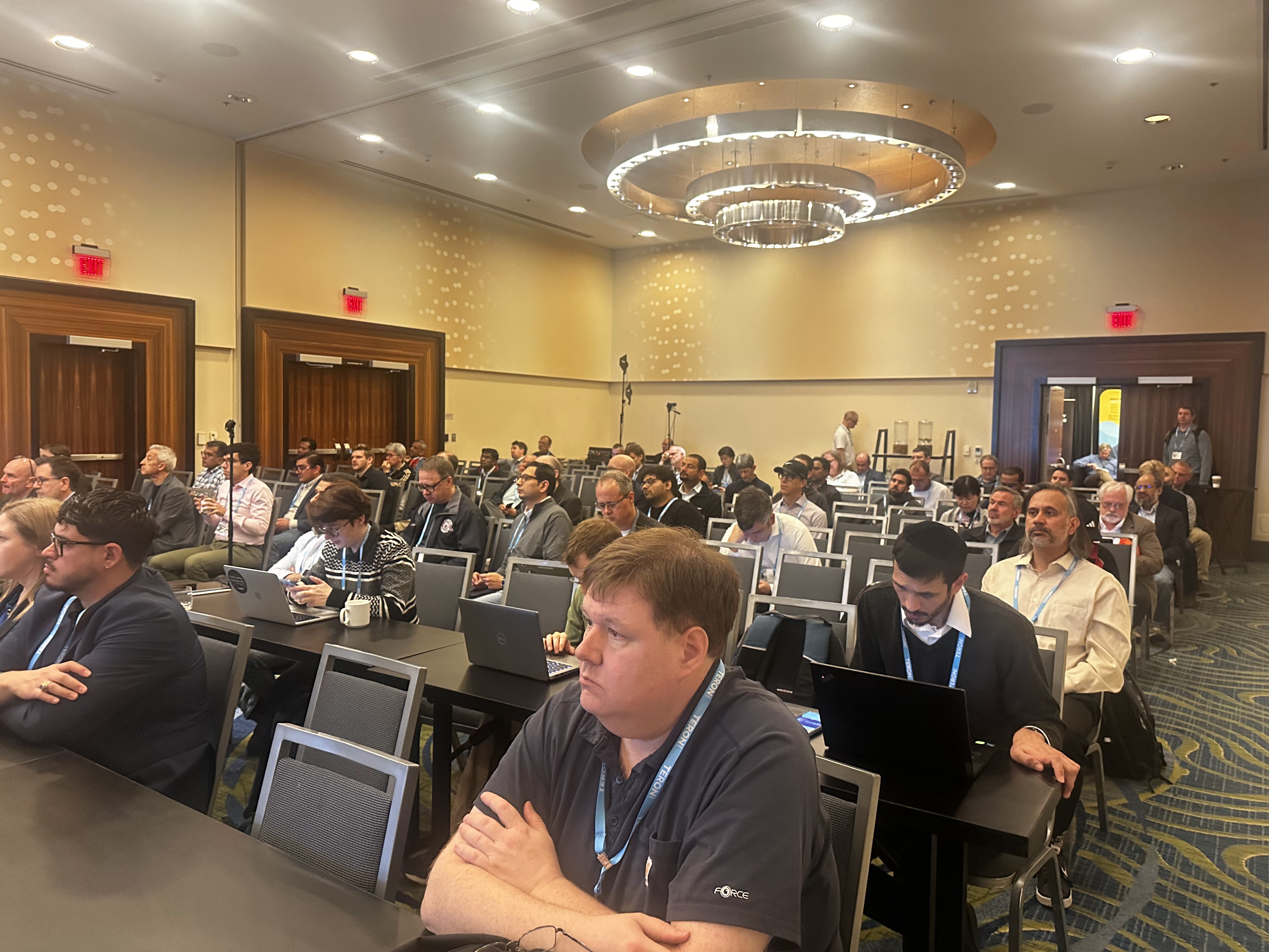 A packed Salon 1 at ICMC26 — rows of attendees listening, many with laptops open, the grand Renaissance-Arlington chandelier above.