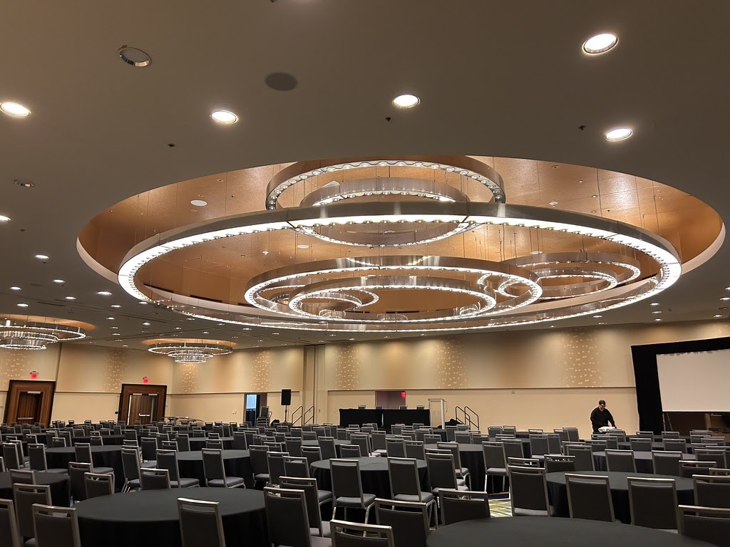 The main ballroom of ICMC26, chairs empty, ring chandelier overhead.