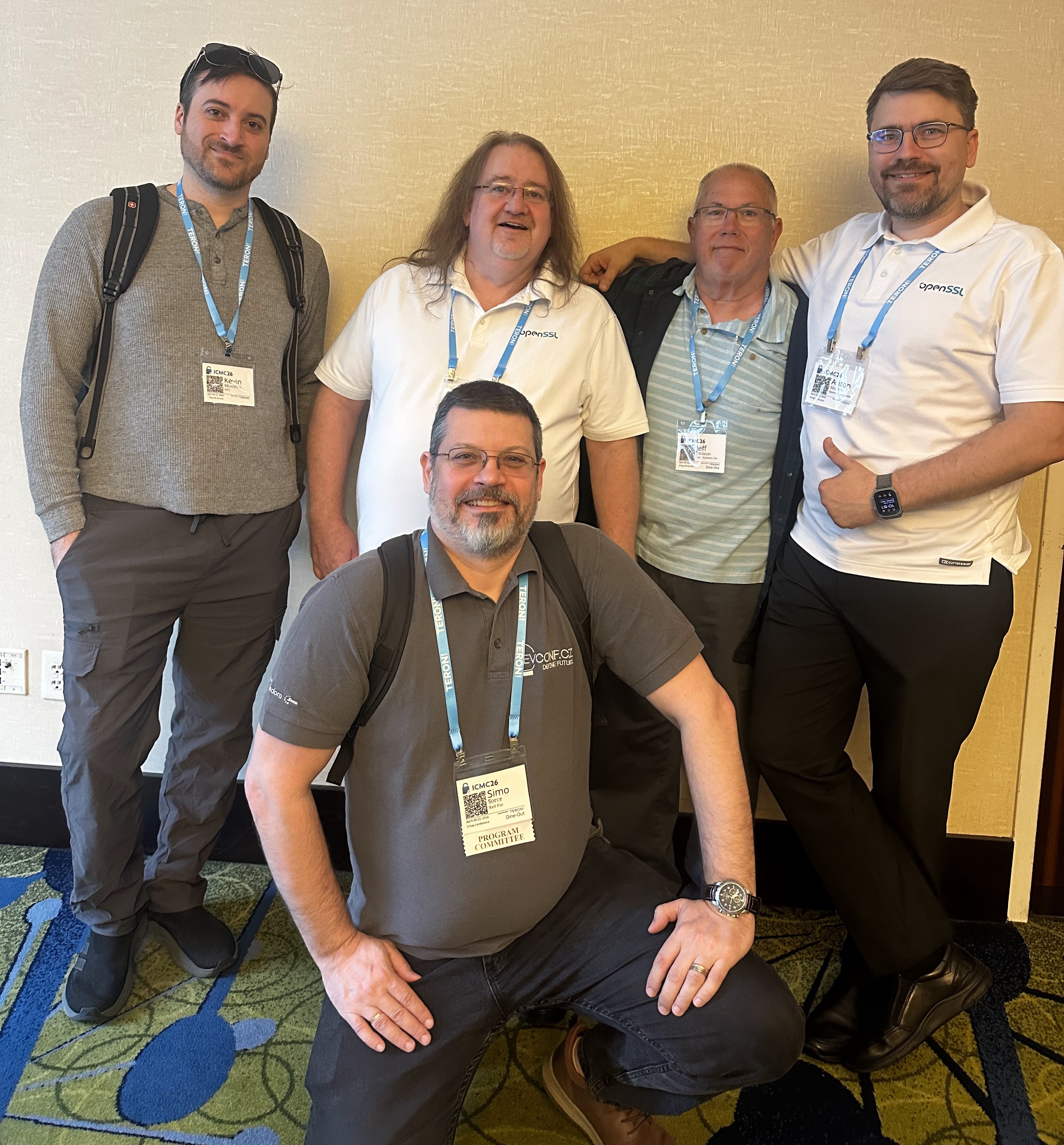 Group photo at the OpenSSL LBC coffee break. OpenSSL Directors with elected Business & Technical Advisory members for large businesses, distributions, and committers — one kneeling in front with a Program Committee lanyard.