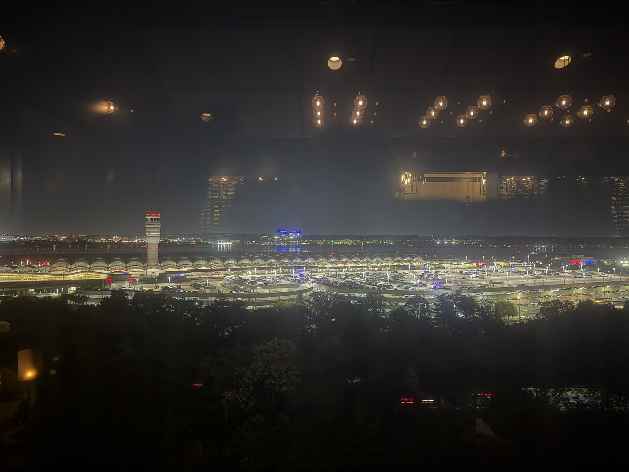 Reagan National Airport at night, seen through a hotel-room window — control tower lit red, terminal canopies, the Potomac beyond.